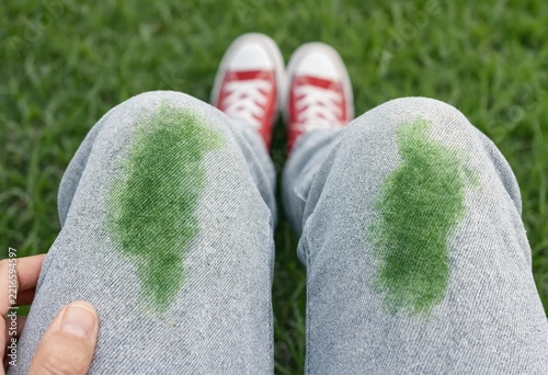 A first-person view of grass stains on blue denim jeans after sitting on a green lawn