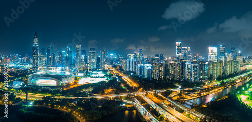 Panoramic aerial view of Shenzhen city skyline illuminated at night, showing modern skyscrapers and glowing roads.