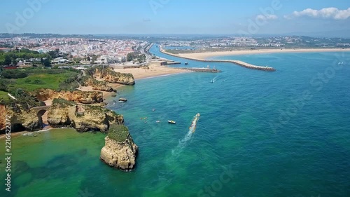 Stunning aerial view of a speedboat navigating the turquoise ocean waters near the picturesque ponta da piedade and camilo beach, with the city of lagos, portugal visible in the background