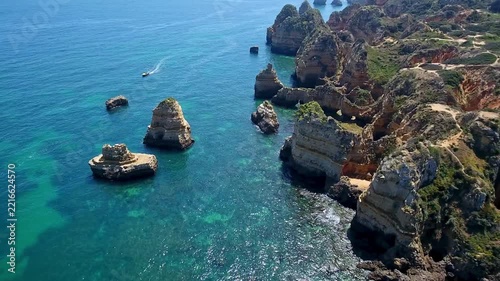 Sunny aerial view of the beautiful ponta da piedade coast, with its impressive rock formations, cliffs, turquoise waters, and a boat navigating the atlantic ocean near lagos, portugal