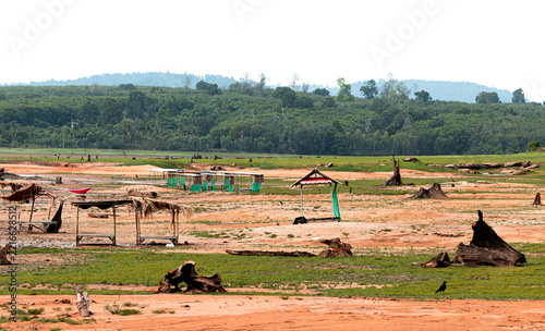 Many shack for temporary resting in open area by freshwater lake. The background is forest and mountain. During dry season and water level has dropped so low that stumps and ground dunes are exposed.