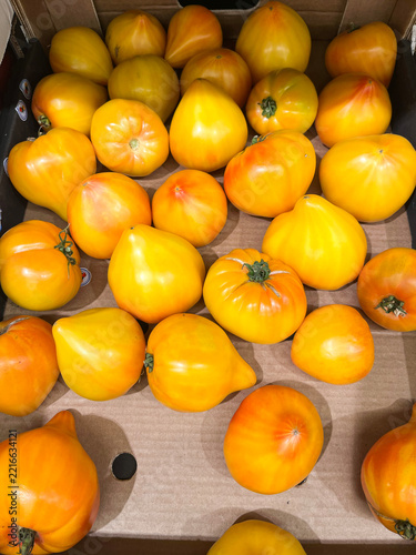 Ripe yellow and orange tomatoes of various shapes are in a supermarket drawer.