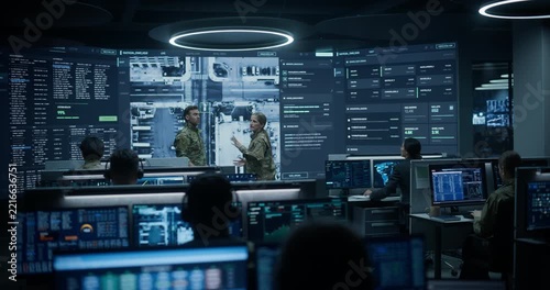 Army Military Surveillance Monitoring Control Room: Two Officers in Uniform Have a Meeting and Talk About Drone Reconnaissance Footage on Screen While Specialists Run AI Big Data Analysis for Defense