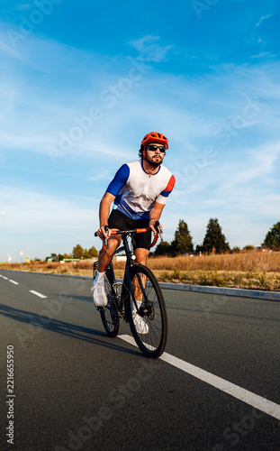 Male cyclist riding bicycle on paved path under clear blue sky.