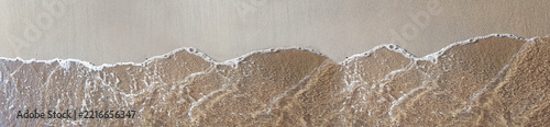 Aerial view of clear ocean water waves washing over wet sandy beach shore in soft sunlight