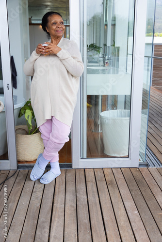 Senior African American woman standing at home doorway holding mug, wearing cardigan, copy space