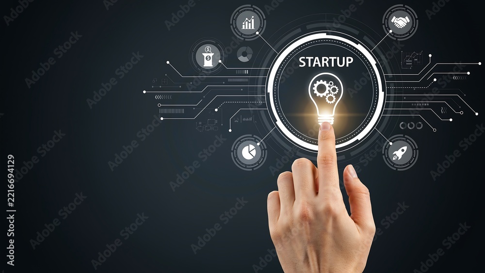 Obraz premium Hand touching lightbulb with startup concept surrounded by digital icons against dark background
