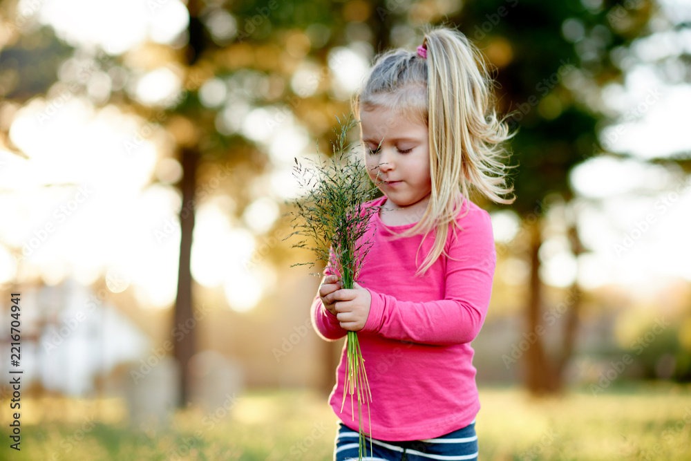 Naklejka premium Park, child and gathering grass for play, holiday and development in environment with bokeh. Outdoor, girl and kid with collection of plants in nature for learning, growth and spring vacation