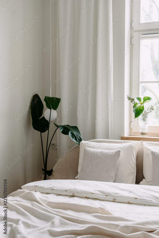 Fototapeta premium Bedroom interior with white bedding, pillows, and green plant on windowsill