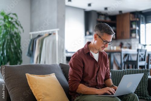 Man working remotely from home using laptop on sofa