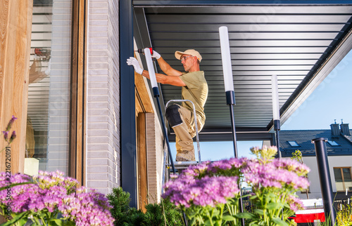 Worker installing a louvered pergola beside a house