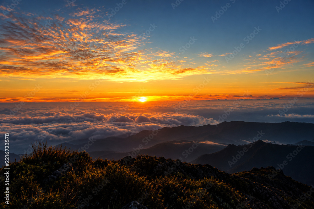 Fototapeta premium Orange horizon above a sea of clouds and rugged peaks