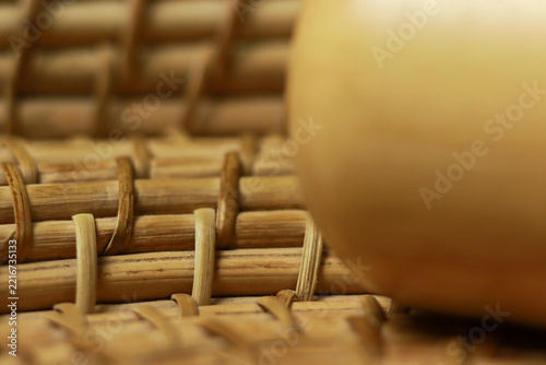 Closeup of a handcrafted wooden mug with a contrasting dark wood handle, placed on a beautifully woven cane or bamboo basket mat.