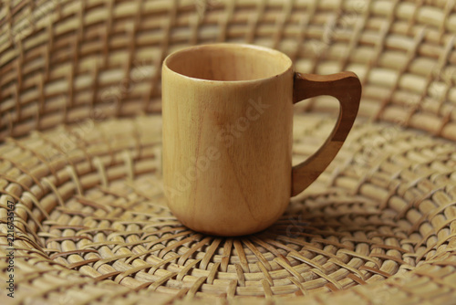 Close up of a handcrafted wooden mug with a contrasting dark wood handle, placed on a beautifully woven cane or bamboo basket mat.