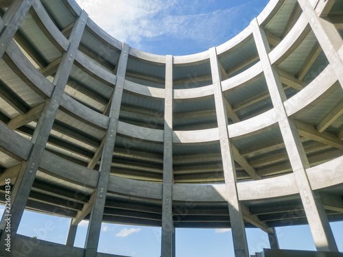 巨大物流センターの円形スロープを真下から見上げたダイナミックな建築美。コンクリート構造物の重厚感と円形吹き抜けから見える青空が印象的な物流インフラとモビリティ構想のイメージ素材。