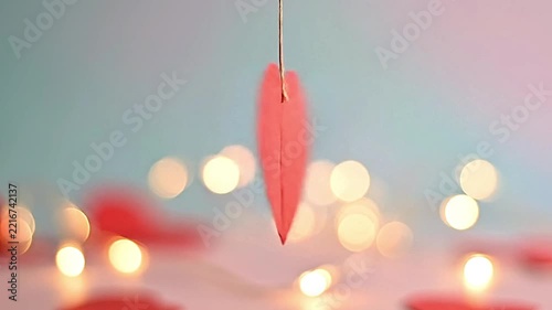 Red paper heart hanging on string rotating slowly with blurred bokeh lights in background motion footage