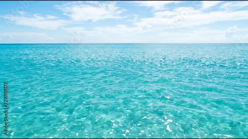 Clear blue water stretches across the horizon under a bright sky with few clouds. The waves gently ripple in the sunlight. It is a tranquil scene at