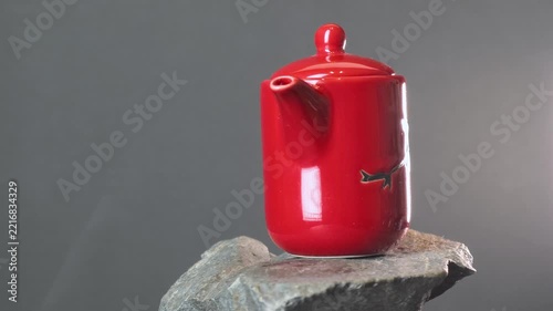 Red ceramic teapot with a glossy glaze on a rough stone slab. Dark grey background, minimalistic still life, tea ceremony, studio lighting