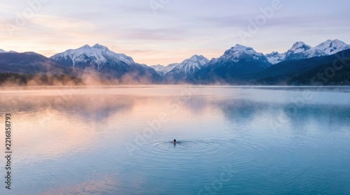 Solitary Swimmer in Calm Lake Reflecting Snowy Mountain Peaks