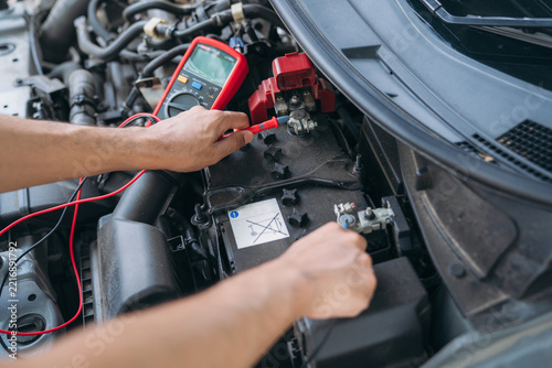 Top view of a mechanic checking car battery voltage with a multimeter