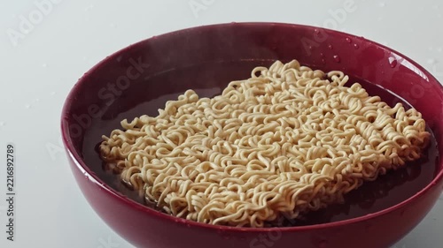 Close-up of boiling water pouring over instant ramen noodles in a red bowl. Cooking process, steam, quick meal, food preparation.