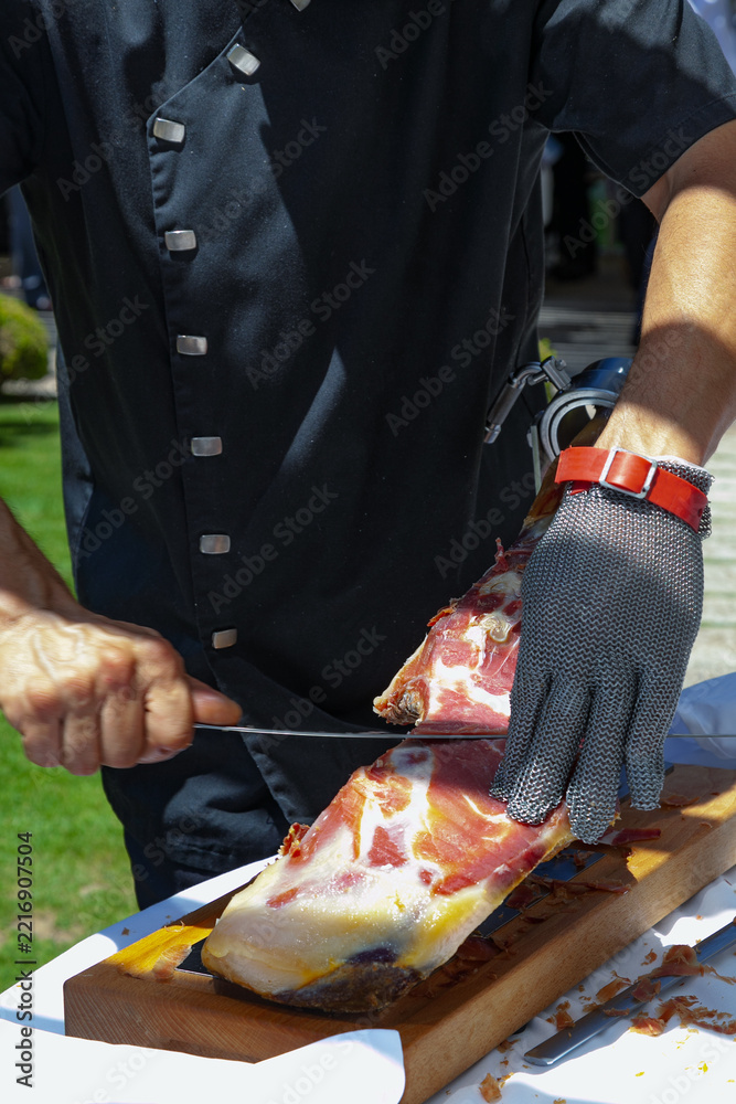 Fototapeta premium Corte de jamón serrano tradicional español con guante protector. Gastronomía tradicional española; tallado de jamón ibérico; chef profesional en cocina gourmet.
