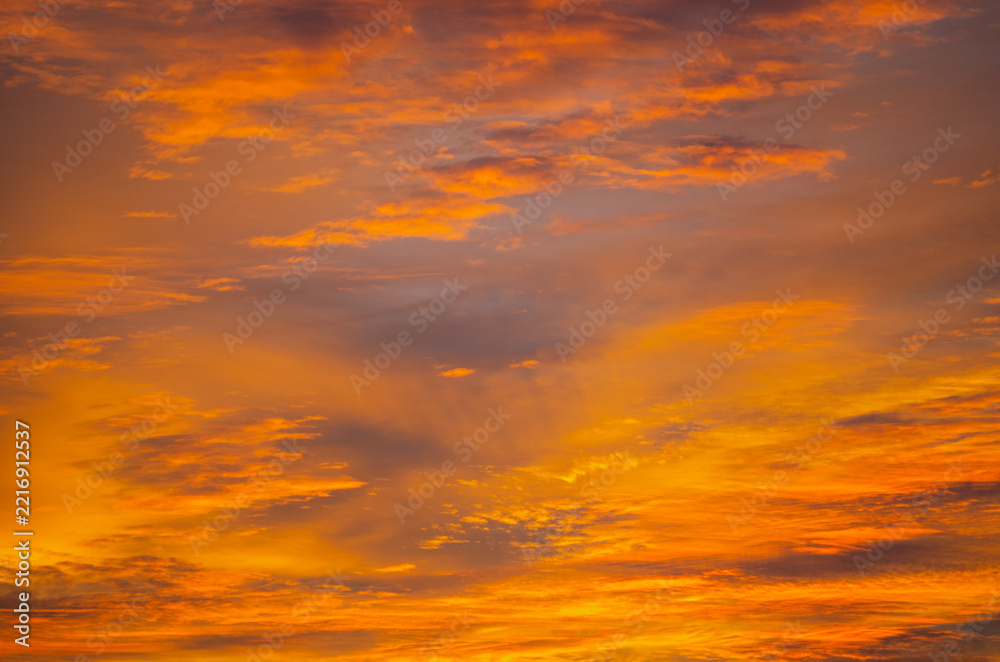 Fototapeta premium Dramatic cloudy sky at sunset glowing with intense orange and golden light, colorful evening clouds and atmospheric natural background 