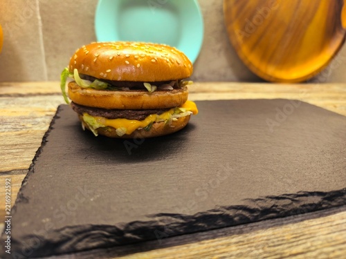 A gourmet grilled burger with fresh tomato slices and aromatic rosemary, served on sesame seed buns on a cutting board