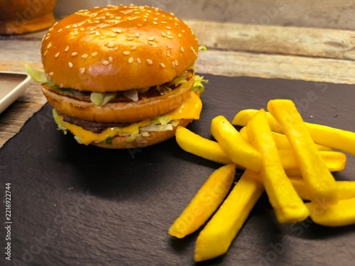 A gourmet cheeseburger with a juicy beef patty, melted cheddar, fresh lettuce, sliced ​​tomatoes and red onions on a serving board.