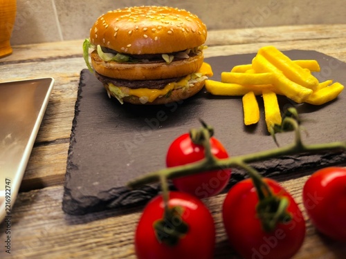 Juicy beef burger on a wooden cutting board with fresh lettuce and tomato slices, French fries and cherry tomatoes
