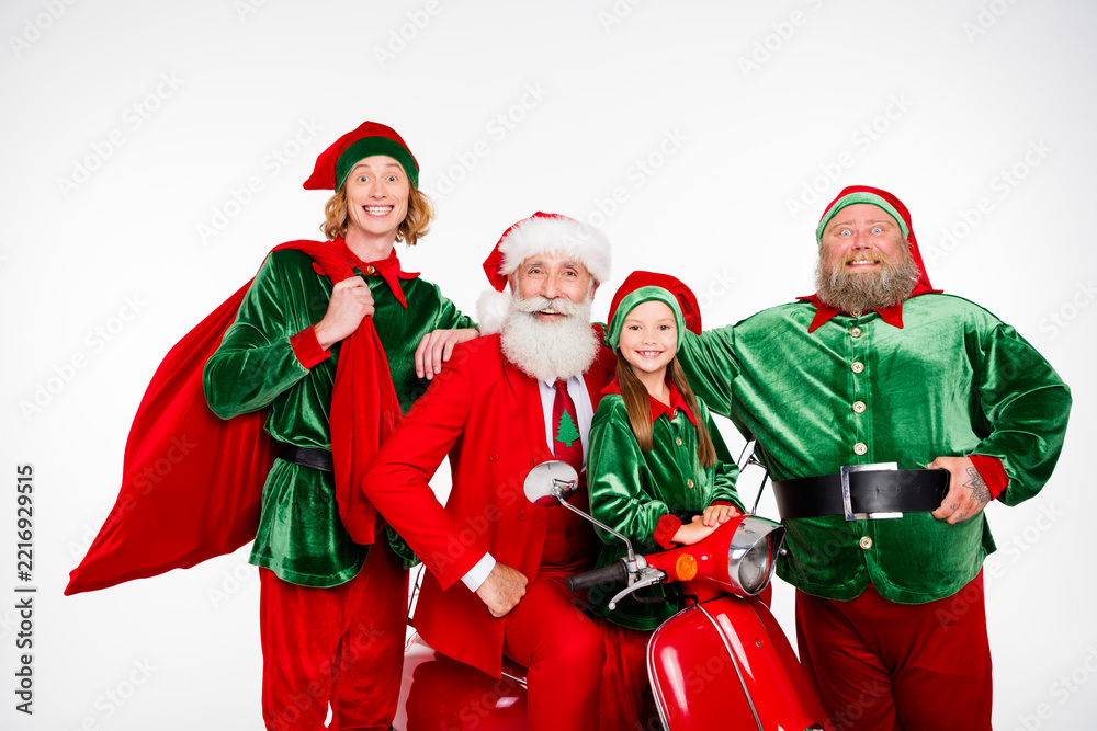 Fototapeta premium Santa Claus with cheerful elves and a young girl on a red scooter celebrating Christmas with festive green and red costumes, laughter, family fun and holiday tradition