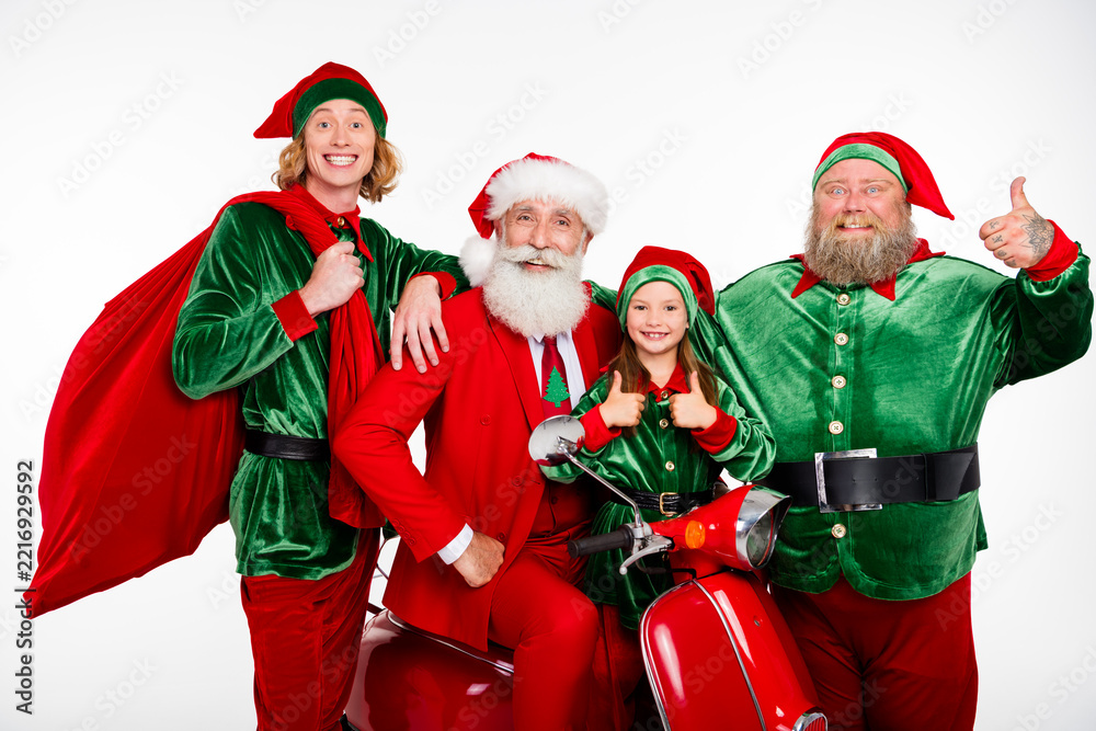 Fototapeta premium Santa and cheerful elves with a child on a red scooter celebrating Christmas together with thumbs up and festive costumes for holiday family fun