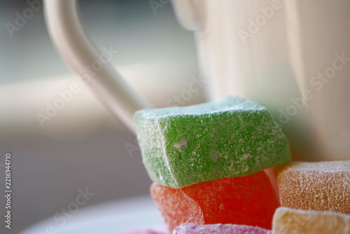 A close-up view of traditional, colorful Turkish delight cubes served with a white Turkish coffee cup.
