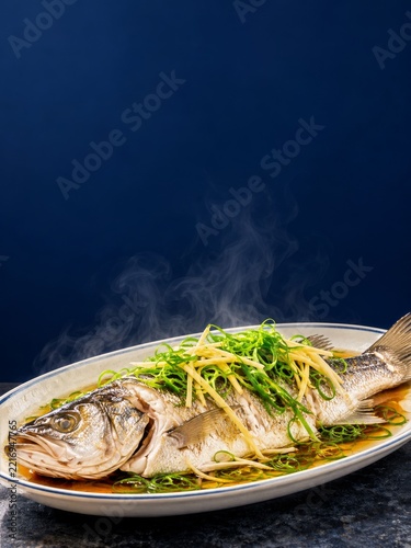 Steamed whole sea bass with ginger and spring onions against navy