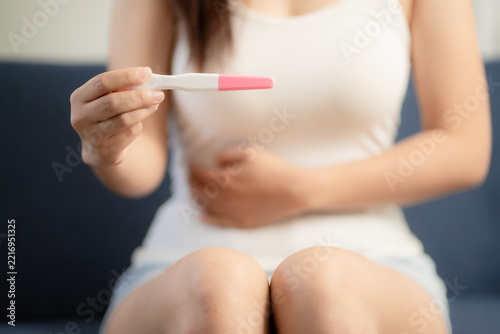 Obraz na plátně Close up of Asian woman holding pregnancy test with thoughtful expression, waiti