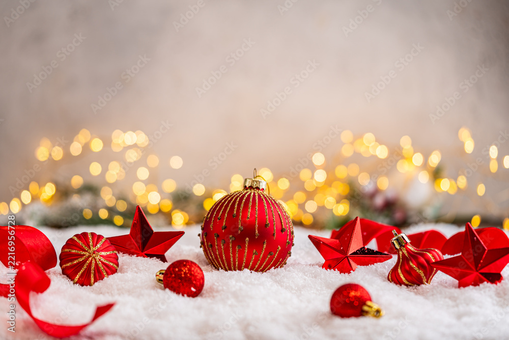 Fototapeta premium A Christmas background featuring red baubles with golden glitter stripes, a star, and ribbon framing wide snowy ground, softly lit by warm twinkling lights with generous copy space.