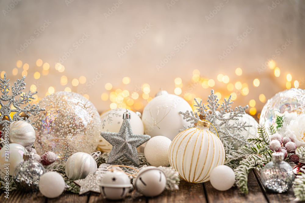 Fototapeta premium A Christmas background featuring elegant white and silver baubles, glittering stars, jingle bells, and snowflakes on rustic wood, set against a warm backdrop with twinkling lights and copy space.