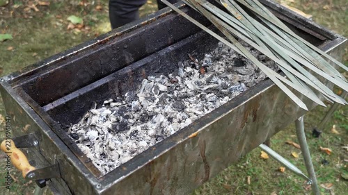 Metal barbecue grill with skewers inside, filled with ash and burned firewood after cooking meat. Close-up of a used grill showing the remains of a barbecue and outdoor cooking process.