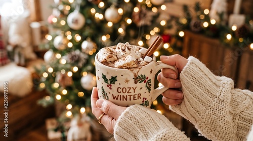 Person holding a cozy winter mug with hot chocolate in front of a blurred christmas tree