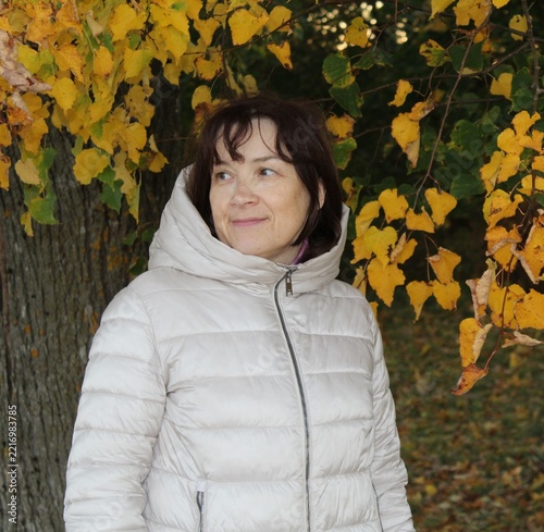 Mature Woman in White Puffer Jacket Smiling in Autumn Park.

