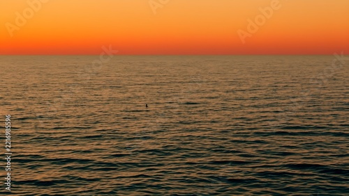 Tiny swimmer far out in gentle sea swell at sunrise, ocean swimming