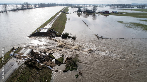 Broken levee with rushing water in a flooded rural landscape  