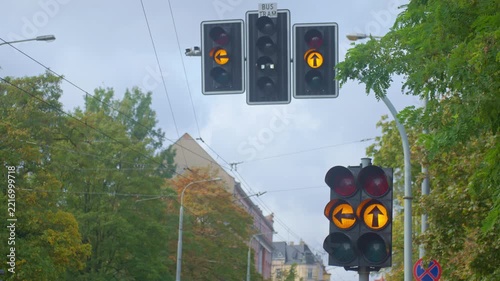 Traffic signals repeatedly flash yellow at city intersection beneath tram power lines