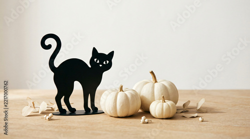 Black cat Halloween concept with Refined black cat silhouette ornament beside white pumpkins on a premium seasonal surface, cheerful Halloween decoration, on a refined studio surface
