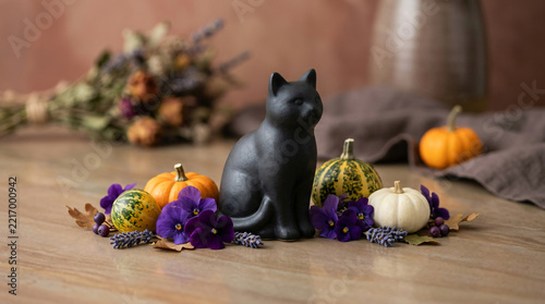 Tiny black cat decoration surrounded by purple flowers and miniature gourds in a playful holiday background for strong seasonal visual impact, with subtle magical glow