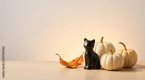 Black cat Halloween colorful party decoration with Small black cat figurine beside pale pumpkins and a curved autumn leaf for seasonal advertising, with warm festive lighting