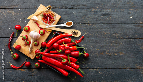Fresh red hot chili peppers, garlic bulb, black peppercorns and paprika powder on dark rustic wooden table. Organic ingredients for spicy Mexican cooking, Hot spices.