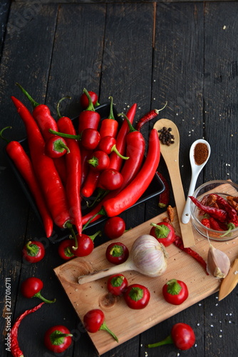 Fresh red hot chili peppers, garlic bulb, black peppercorns and paprika powder on dark rustic wooden table. Organic ingredients for spicy Mexican cooking, Hot spices.
