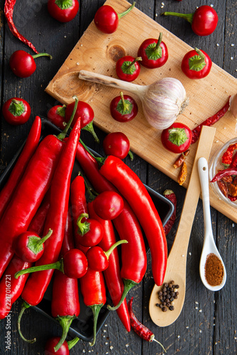 Fresh red hot chili peppers, garlic bulb, black peppercorns and paprika powder on dark rustic wooden table. Organic ingredients for spicy Mexican cooking, Hot spices.
