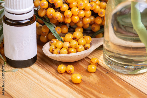  Sea buckthorn berries on branch with oil bottle and wooden spoon on green background. Organic herbal medicine concept for immunity boost